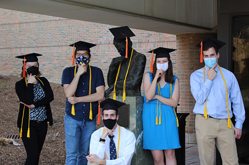 group of masked students in grad cap and gown pose around the statue of Claude Shannon on North Campus